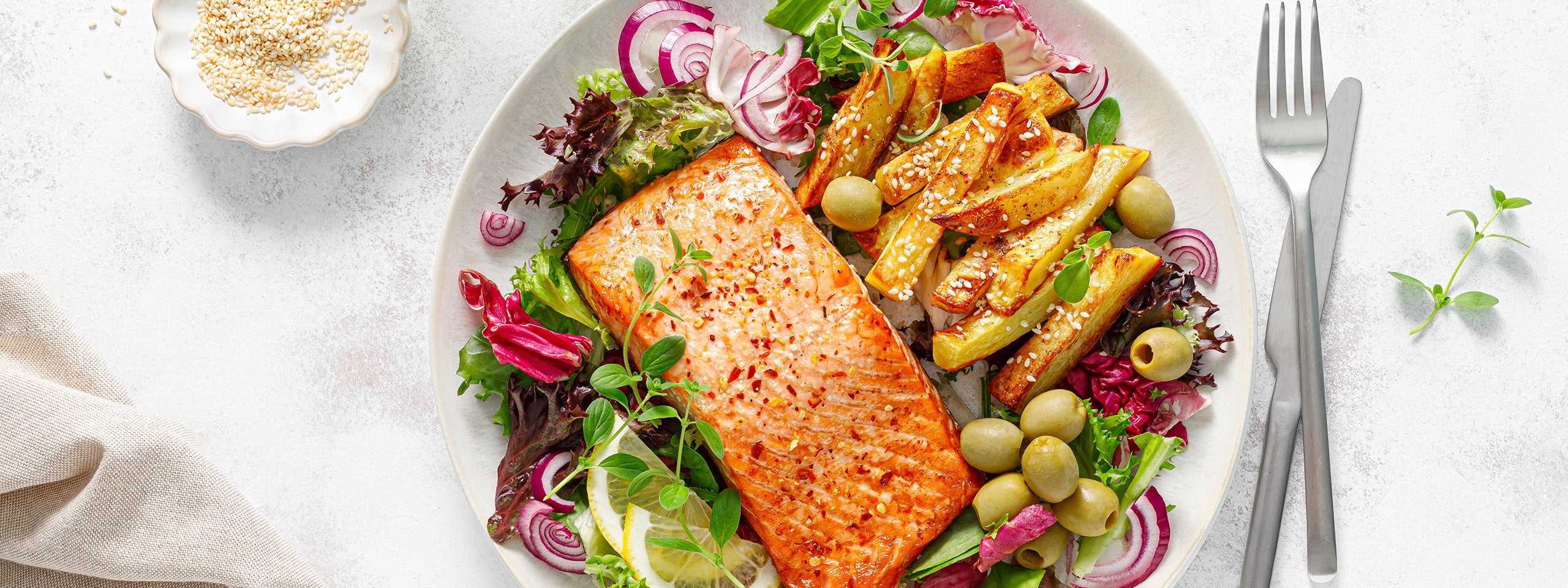 Ein Teller mit Lachs, Kartoffel-Spalten und Salat, daneben Besteck.