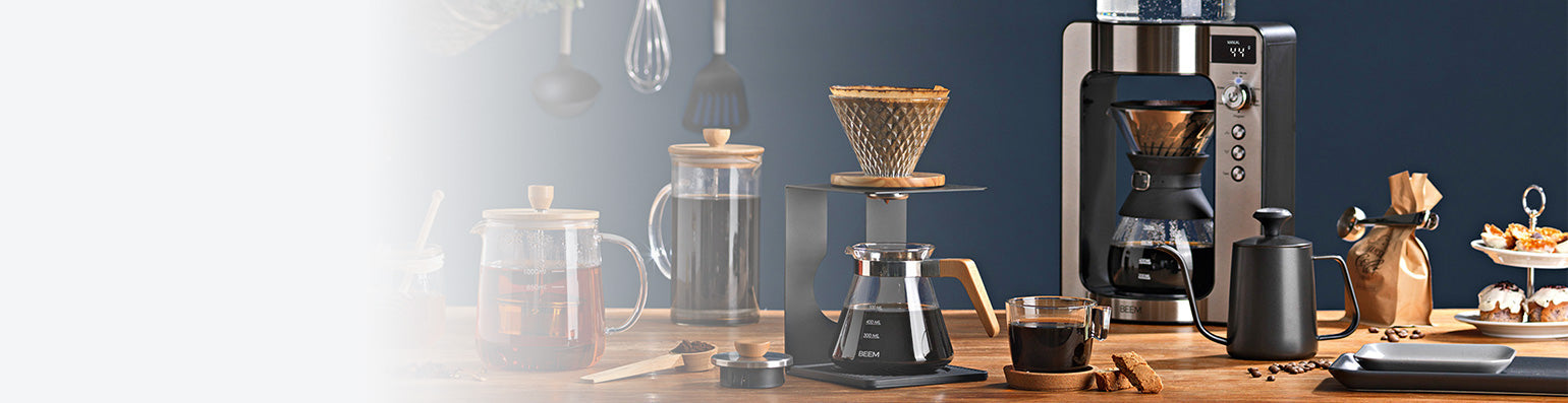 Verschiedene Produkte von BEEM auf einem Holztisch: Teekanne, Pour Over, Frensh Press, Kaffeemaschine und Kaffeemühle.