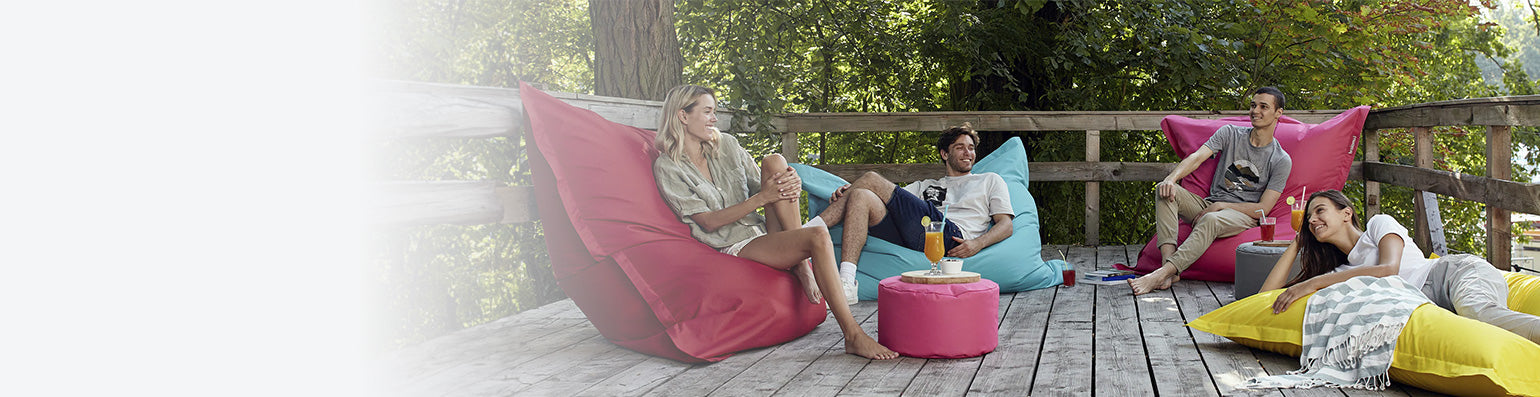 Eine Gruppe Männer und Frauen liegen und sitzen auf LUMALAND XXL Sitzsäcken für den Outdoor-Bereich auf einer Terrasse.