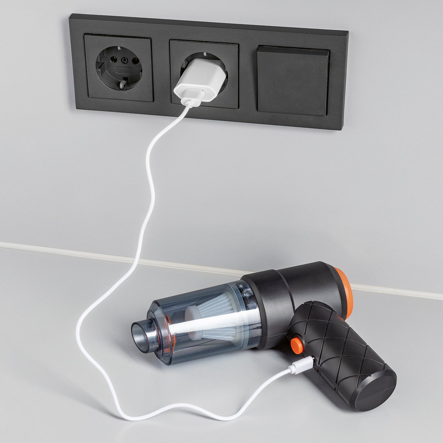 2in1-Akkusauger mit Saug- und Gebläsefunktion mit transparentem Behälter, ergonomischem Griff und USB-Ladekabel an Steckdose angeschlossen.