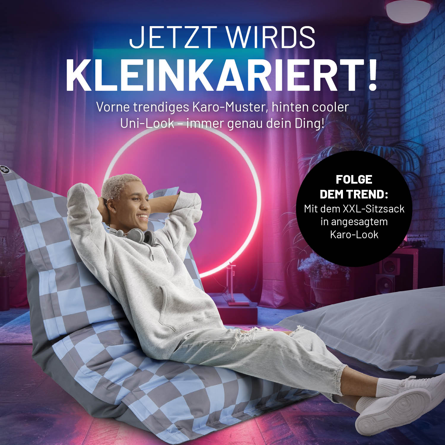 Person entspannt auf XXL-Sitzsack Karo - Blau/Grau mit trendigem Karo- und Uni-Design in modernem Raum mit Neonlicht.