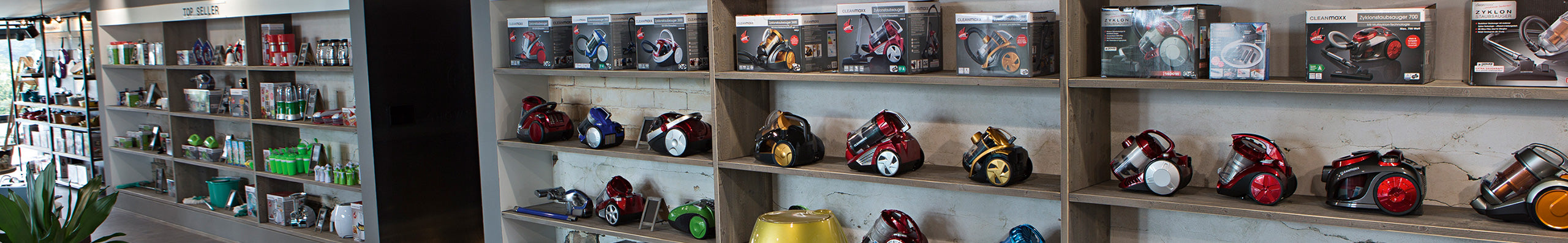 Regale im Showroom der DS Produkte GmbH, gefüllt mit Staubsaugern, Verpackungen und Haushaltswaren unter dem Label „Top Seller“.