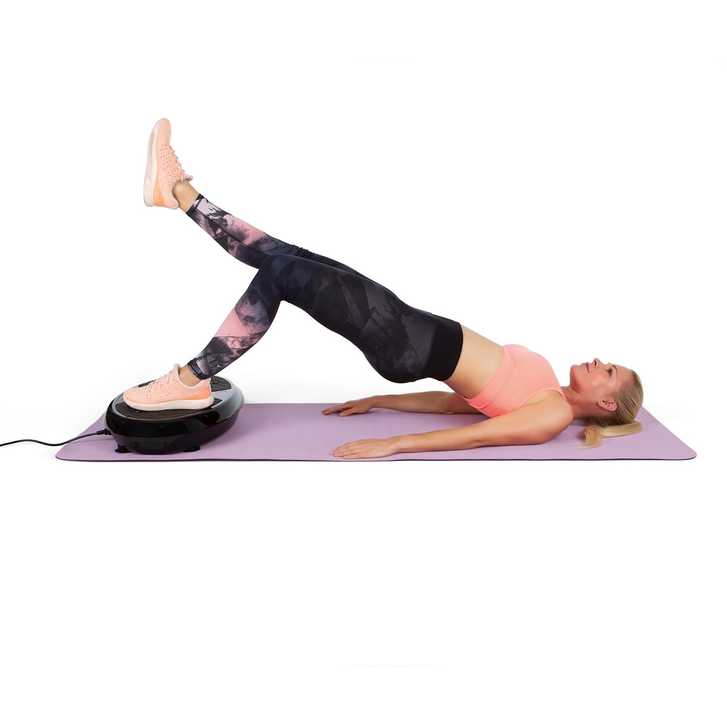 Frau trainiert auf Vibrationstrainer mit einem Bein auf Gerät für effektives Ganzkörpertraining zu Hause.