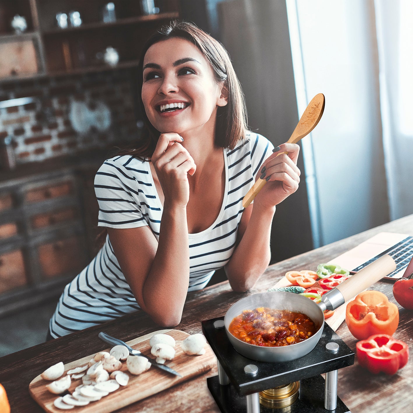 Frau kocht mit dem Tisch-Kochset für bis zu 2 Personen - Edelstahl/schwarz auf dem Tisch und hält einen Kochlöffel aus Holz.