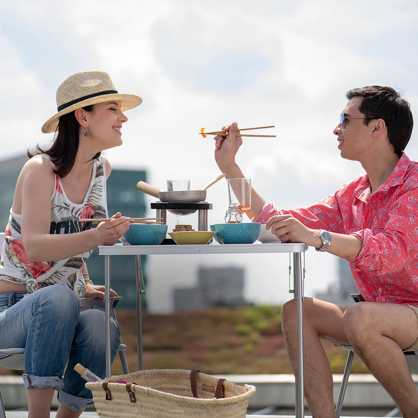 Zwei Personen genießen draußen eine Mahlzeit mit dem Tisch-Kochset für bis zu 2 Personen - Edelstahl/schwarz bei sonnigem Wetter.