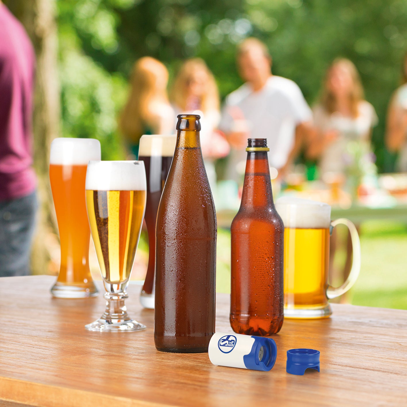 Bier-Aufbereiter im FC Schalke 04-Design 3er-Set neben Bierflaschen auf Holztisch im Freien mit Glasbier im Hintergrund