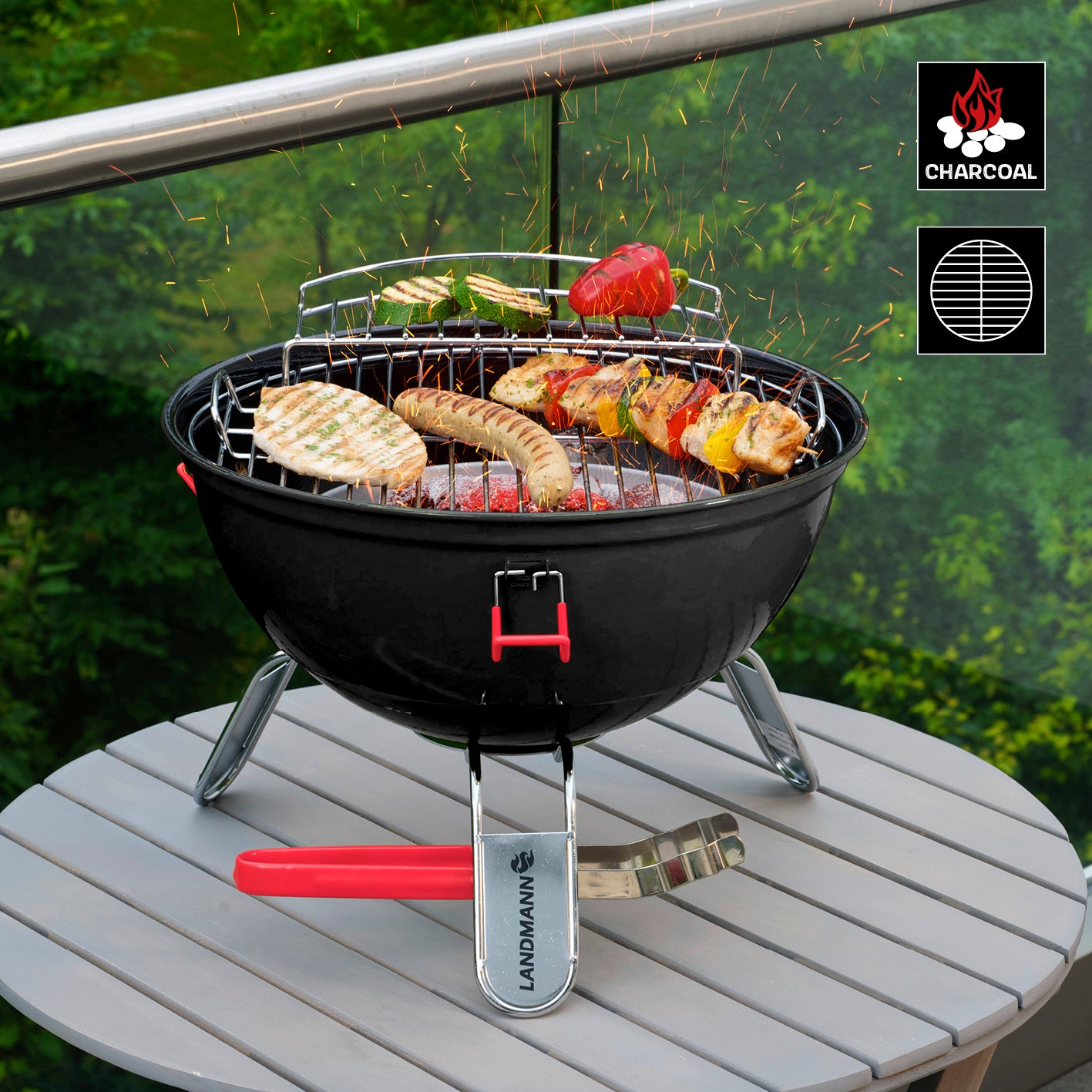 Piccolino King Holzkohlegrill mit pulverbeschichtetem Deckel, gummierten Klammern und Edelstahl-Grillzange auf Tisch im Garten.