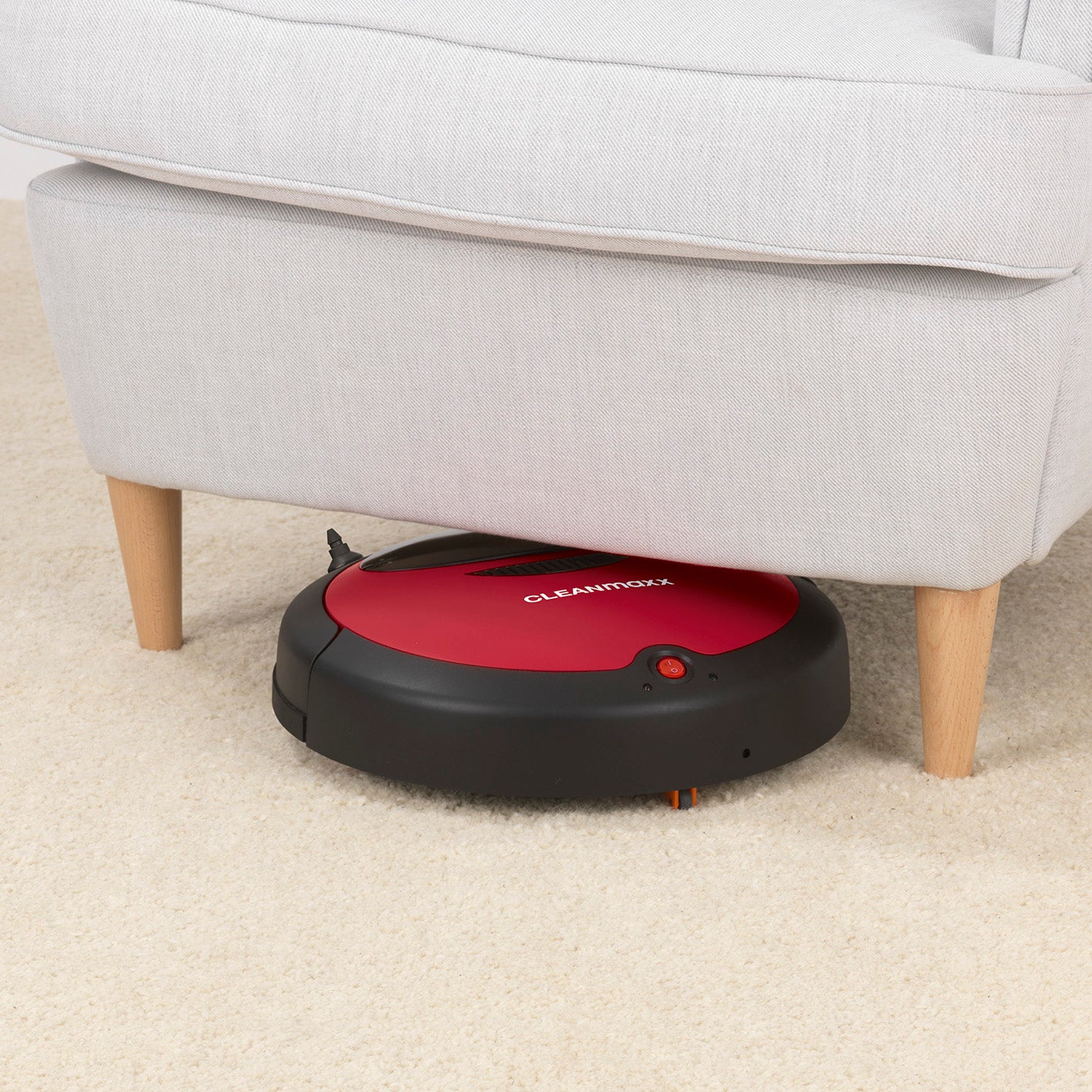 Saugroboter 2in1 - rot/schwarz reinigt Teppichboden unter einem hellen Sofa mit sensorgesteuerter Navigation.
