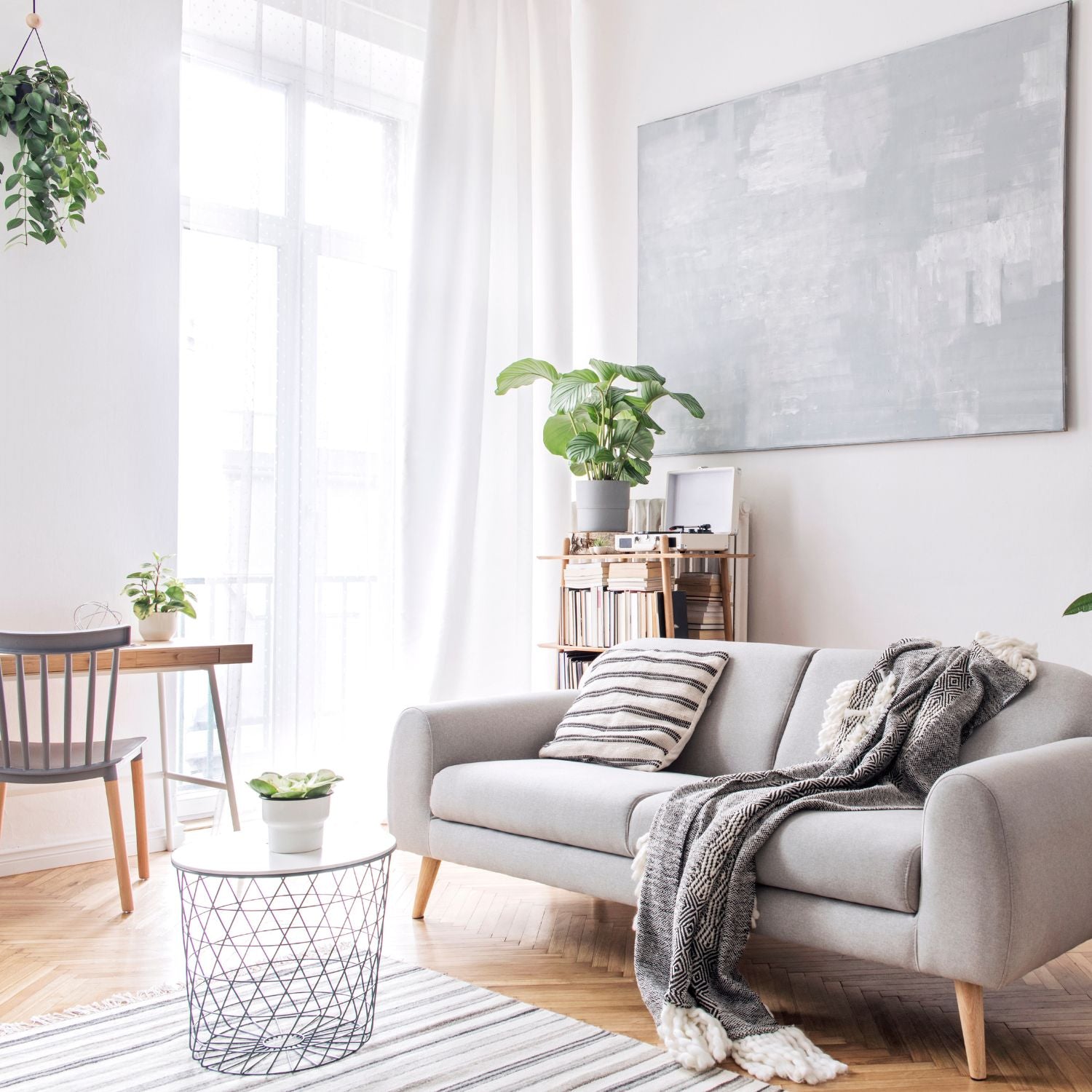 Helles Wohnzimmer mit grauem Sofa, Kuscheldecke, Pflanzen und minimalistischer Deko im skandinavischen Stil.