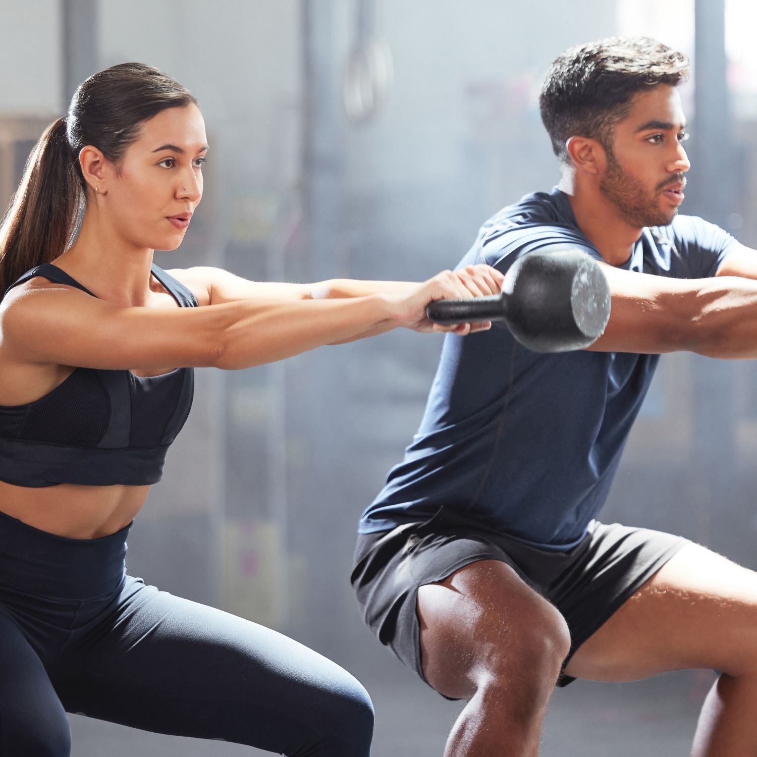 Zwei sportliche Personen machen gemeinsam Kniebeugen mit einer Hantelstange im Fitnessstudio – fokussiertes Training.