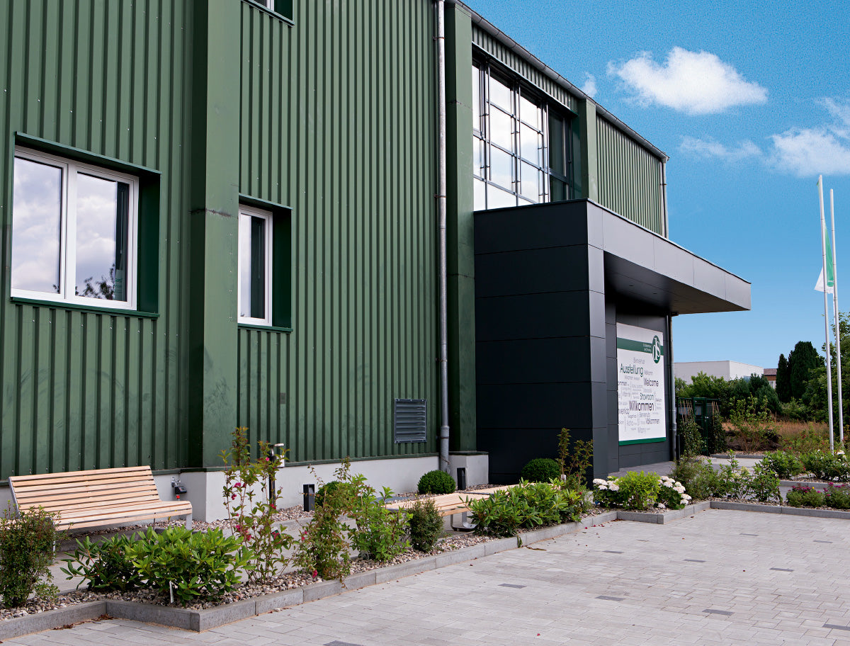 Grünes Firmengebäude der DS Produkte GmbH mit moderner Eingangsfassade, gepflegtem Vorgarten und Willkommensschild.