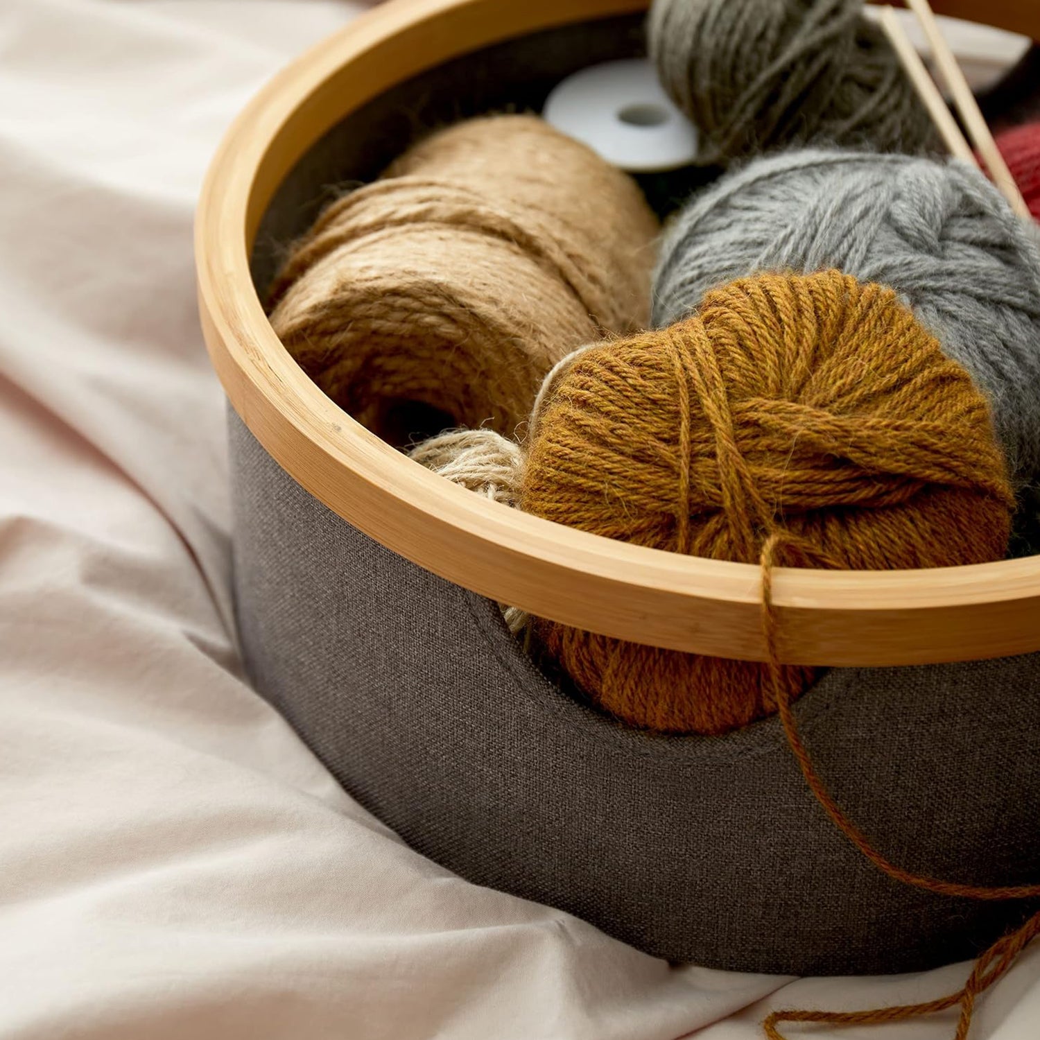 Bambus-Rahmen Aufbewahrungsbox rund - 3er-Set - Rosa mit grauem Stoff und Bambusrahmen gefüllt mit Wollknäueln und Stricknadeln.