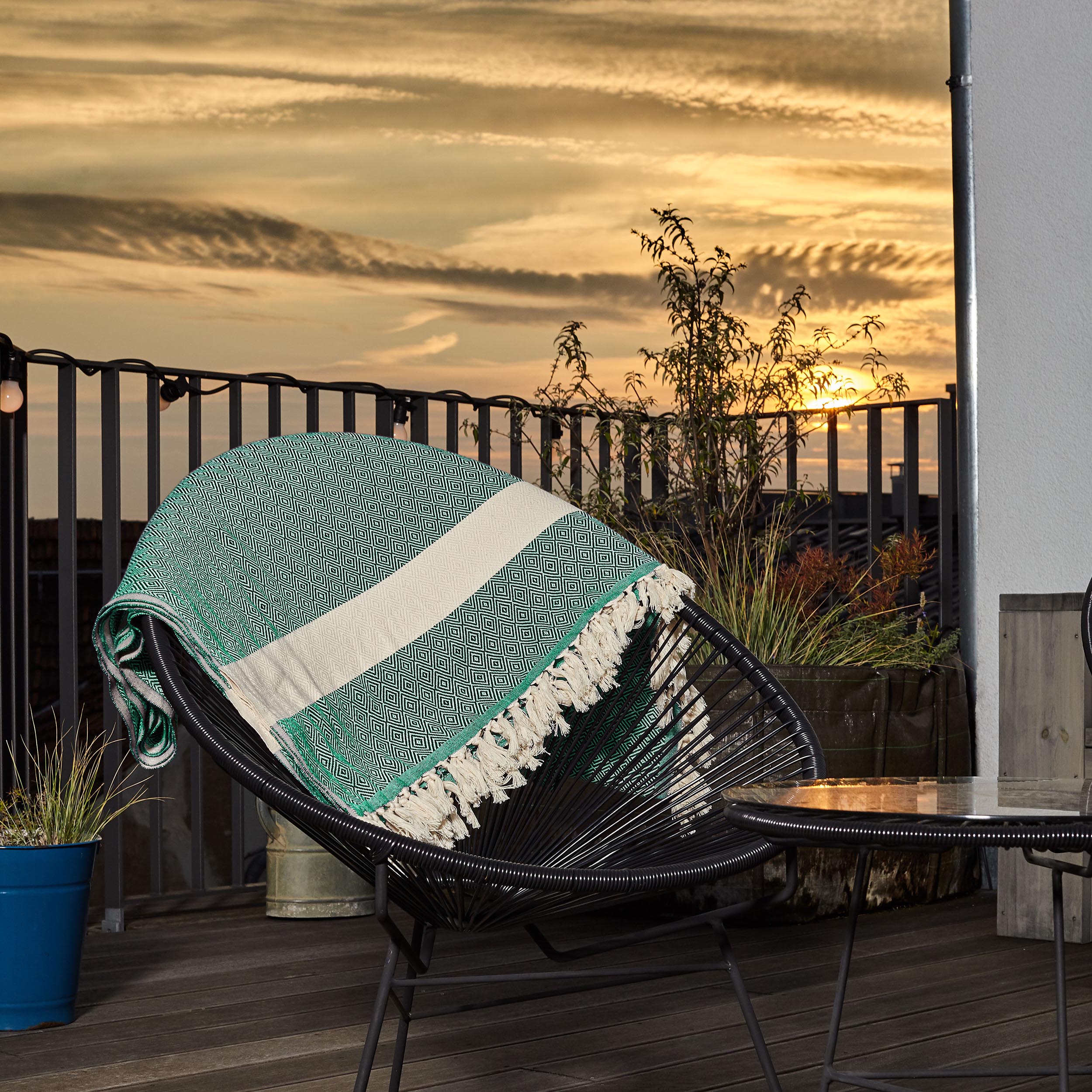 Baumwolldecke / Tagesdecke aus 100 % Baumwolle - ca. 200 x 240 cm in Grün auf Stuhl im Außenbereich bei Sonnenuntergang.