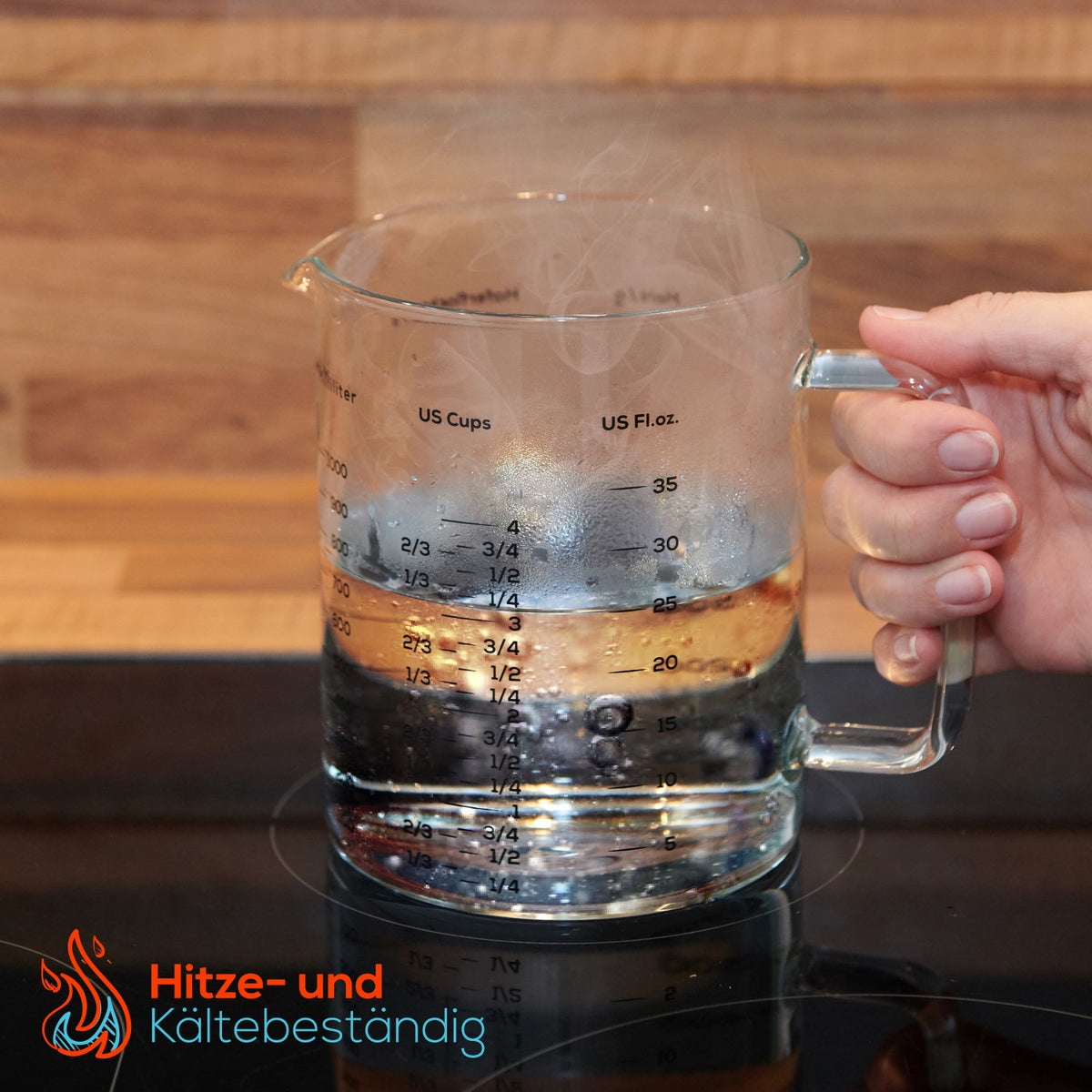 Messbecher - Glas - 1 L & 500 ml - 2er Set mit hitze- und kältebeständigem Glas, gefüllt mit Wasser auf Herdplatte, Hand hält Griff